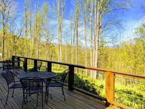 Eine Holzterrasse mit Tisch und Stühlen, mit Blick auf einen bewaldeten Bereich.