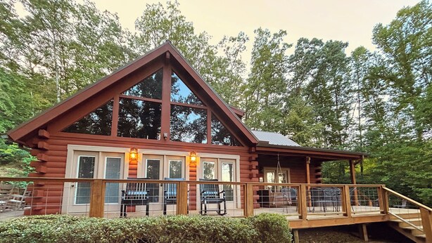 A log cabin with a large deck, multiple windows, and a staircase leading to the entrance.
