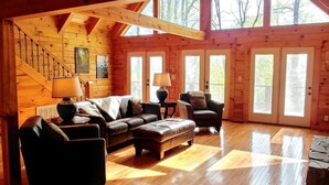 A log cabin interior with a wooden staircase, a leather sofa, a coffee table, and a fireplace.