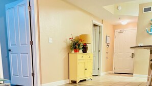 A hallway with wooden flooring, a yellow cabinet with a plant, and a door with a blue frame.