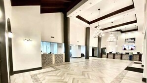 A spacious lobby with a herringbone-patterned floor, large pillars, and a modern chandelier.