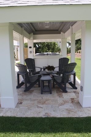 A covered patio area with four Adirondack chairs and a small table, surrounded by white pillars and a tiled floor. - NEW*** COUPLES RETREAT IN DUCK (Duck)
