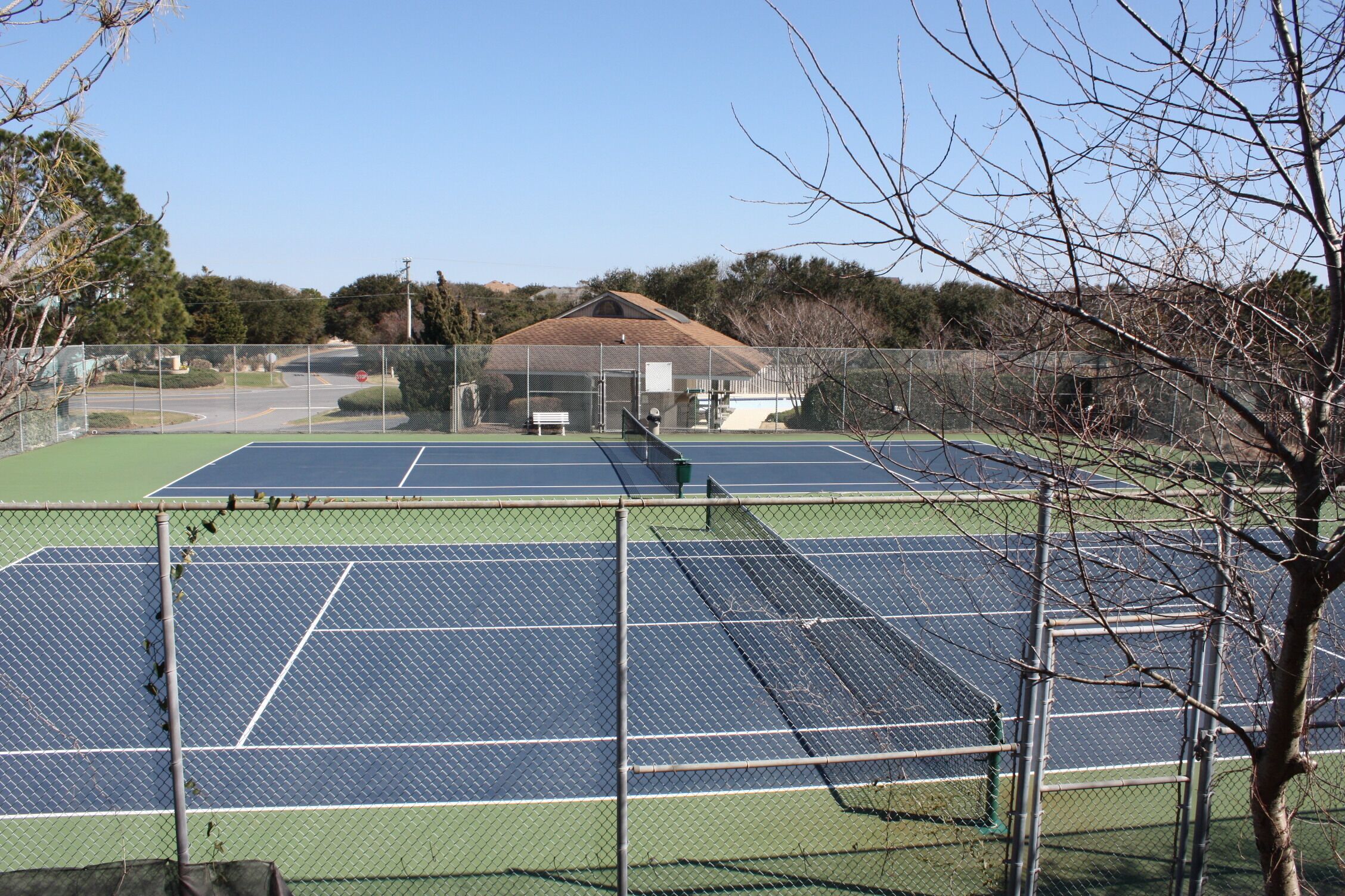 Una cancha de tenis con valla, una banca y un edificio al fondo.