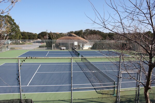 Una cancha de tenis con valla, una banca y un edificio al fondo.