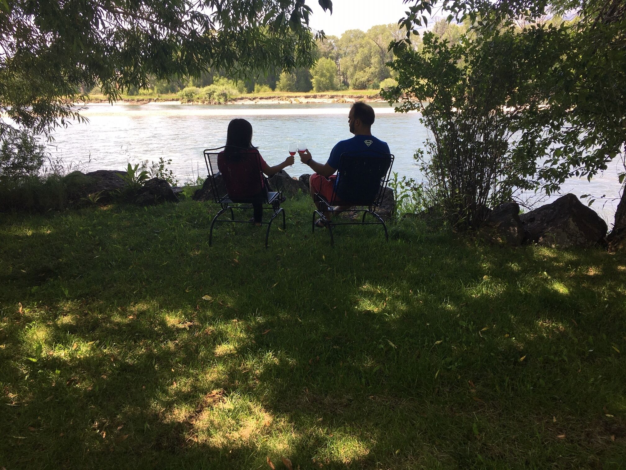 Due persone sedute su sedie di fronte a un fiume, circondate da erba e alberi.