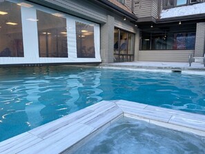 A swimming pool with a tiled deck, large windows, and a building with a brick facade.