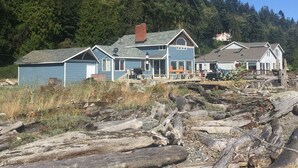 A two-story house with a porch, surrounded by forested hills. - Anchor Away, Whidbey Island Beachfront Getaway (Clinton)