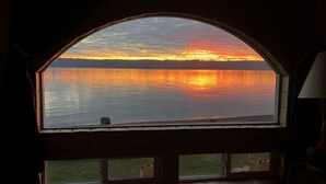A room with a large arched window overlooking a lake at sunset. - Anchor Away, Whidbey Island Beachfront Getaway (Clinton)