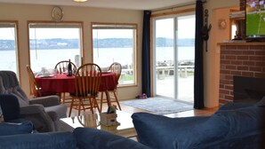 A living room with a blue sofa, a dining table with chairs, and a fireplace. - Anchor Away, Whidbey Island Beachfront Getaway (Clinton)