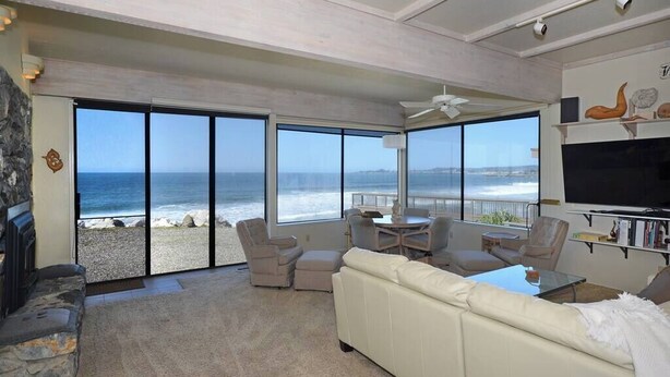 A spacious living room with a large window overlooking the ocean, a fireplace, and a television on the wall. - Villa Vista Lower (Santa Cruz)