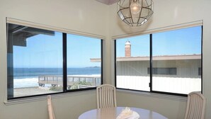 A dining area with a table and chairs, large windows with a view of the ocean and a lighthouse, and a hanging light fixture. - Villa Vista Lower (Santa Cruz)