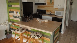 Una cocina con una isla de madera, armarios blancos y un microondas. Hay dos taburetes con cojines estampados.