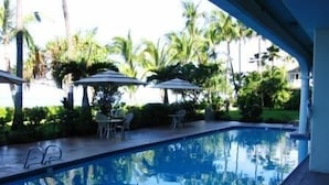 Una piscina con borde de baldosas, rodeada de palmeras y mobiliario exterior.