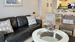 A living room with a black leather sofa, patterned armchairs, a coffee table, and a painting on the wall.