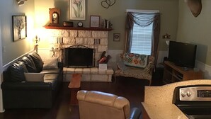 A living room with a fireplace, a sofa, a television, and a kitchen area with a stove. - ACE OF HEARTS The perfect getaway! Only 3.5 miles from Main Street. (Fredericksburg)