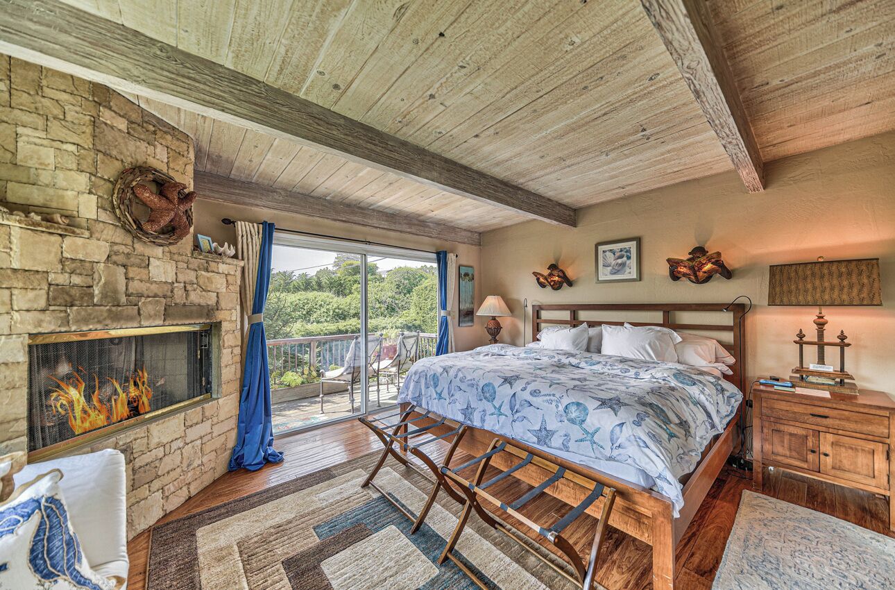A bedroom with a stone fireplace, a bed with a blue floral bedspread, a wooden headboard, and a nightstand with a lamp.