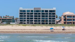 Ein mehrstöckiges Hotel mit Balkonen, gelegen an einem Strand mit sandigem Ufer und Meerblick.