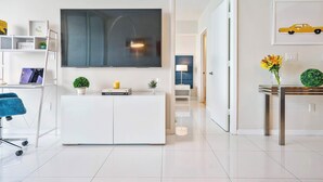 Un salon moderne avec un grand téléviseur à écran plat, une console blanche, un fauteuil bleu et une petite table d’appoint sur laquelle est posé un vase.