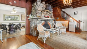 Ein gemütliches Wohnzimmer mit Kamin aus Stein, Korbmöbeln und einer Holztreppe.