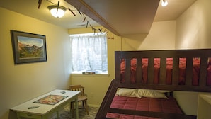 A room with a bunk bed, a desk with a board game, a chair, a window with curtains, and a framed picture on the wall. - Glacier National Park family-friendly flat (Columbia Falls)