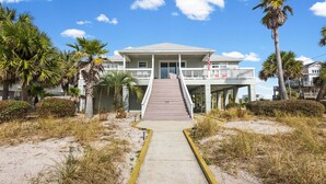 A beachfront property with a two-story building, a concrete pathway leading to the entrance, and surrounding palm trees. - 🌞 The Sunshine Gulfside | Sleeps 22 w/ Private Pool + Steps to Beach (Pensacola Beach)