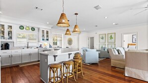 A spacious kitchen with a central island, wooden flooring, and wicker pendant lighting. - 🌞 The Sunshine Gulfside | Sleeps 22 w/ Private Pool + Steps to Beach (Pensacola Beach)