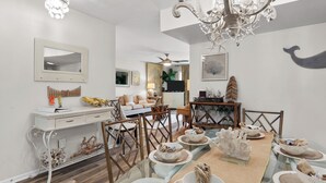 Un coin repas avec une table en verre, des chaises blanches et un lustre.