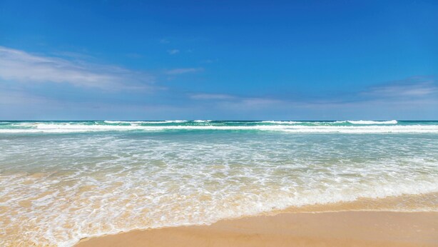 Une plage à l’eau d’un bleu limpide et au rivage sablonneux.