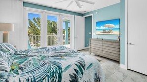 A bedroom with a bed, a ceiling fan, a TV, and a view of the outdoors.