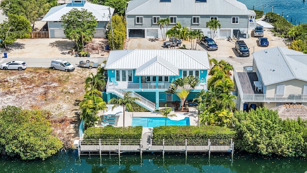 A large house with a pool, surrounded by palm trees and a dock.