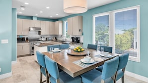 A modern kitchen with light-colored cabinets, a central island, and a dining area with blue chairs and a wooden table.