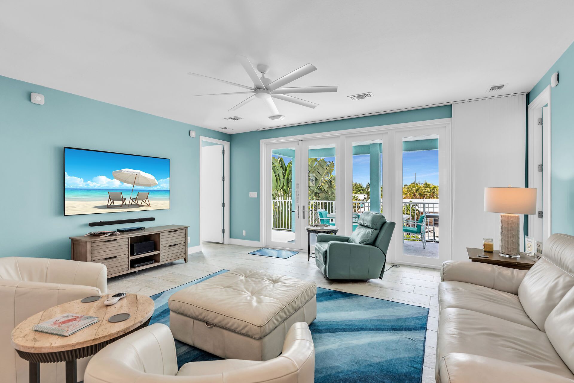 A spacious living room with a television, leather sofas, a coffee table, and a ceiling fan.