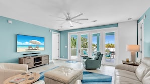 A spacious living room with a television, leather sofas, a coffee table, and a ceiling fan.