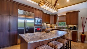 A modern kitchen with dark wood cabinets, stainless steel appliances, a granite island with bar stools, and a decorative vase.