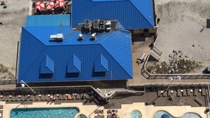 An aerial view of a resort with a large pool area, multiple sun loungers, and a covered seating area with umbrellas. - Oceanfront Penthouse Suite - Prince Resort (Myrtle Beach)