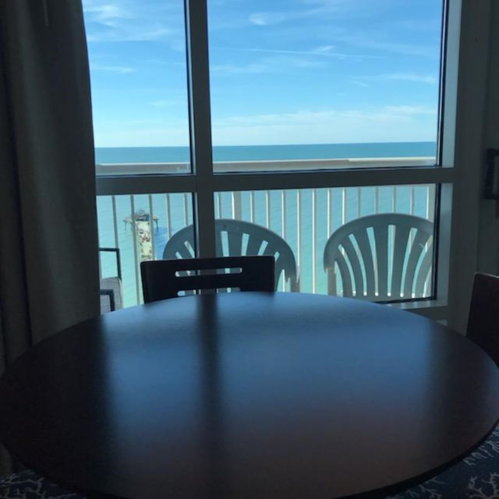 Une table ronde avec deux chaises, dans une pièce dotée d’une grande fenêtre donnant sur l’océan.