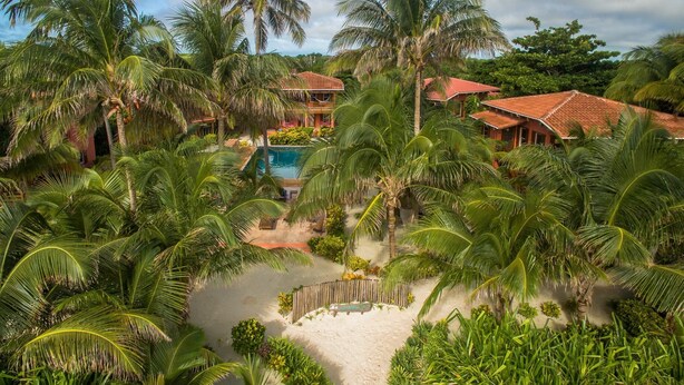 Un resort tropical con piscina, palmeras y un edificio de techo rojo.