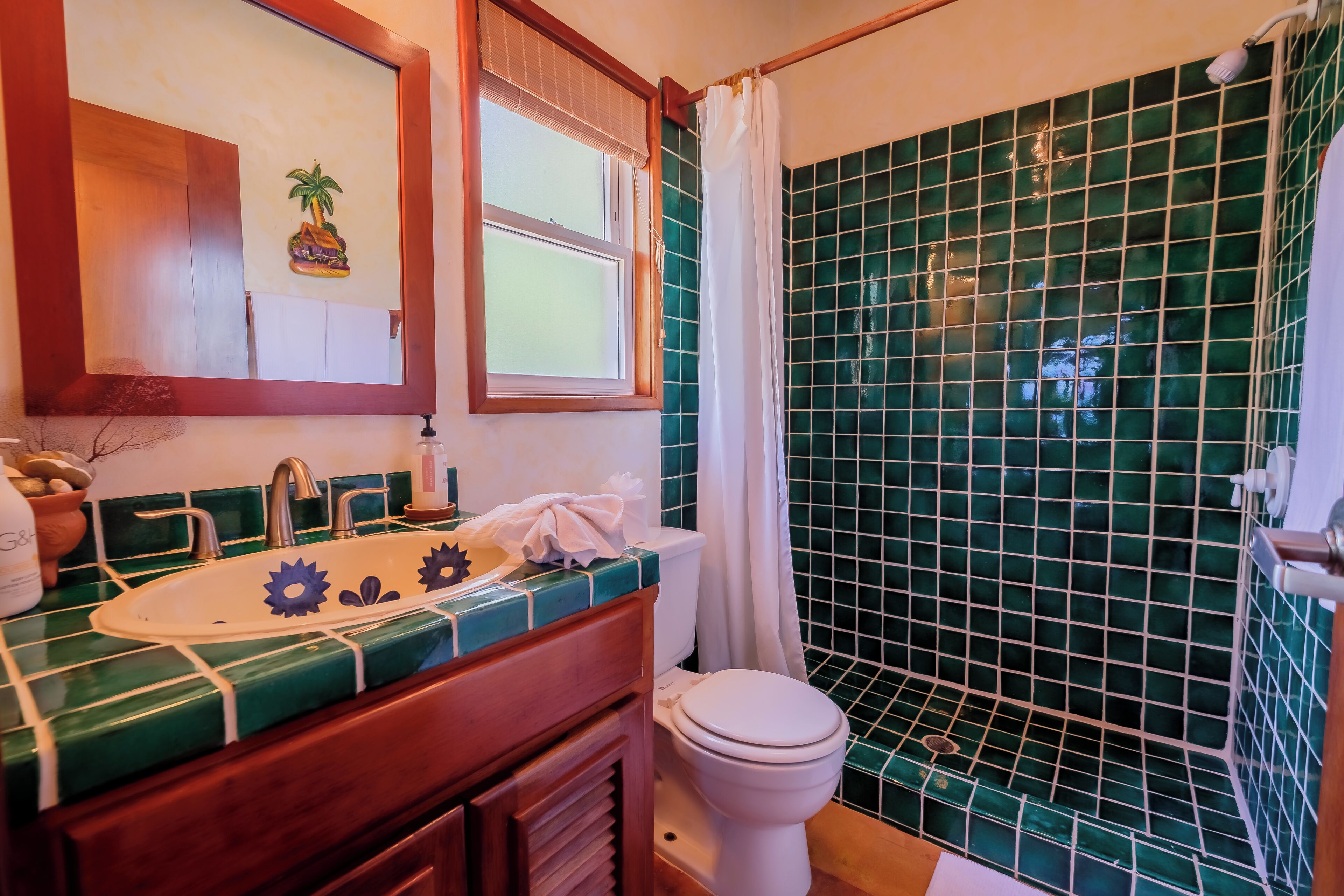 Une salle de bain avec une douche aux carreaux verts, un lavabo blanc orné de motifs bleus décoratifs et un meuble-lavabo en bois.