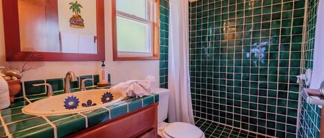 Une salle de bain avec une douche aux carreaux verts, un lavabo blanc orné de motifs bleus décoratifs et un meuble-lavabo en bois.