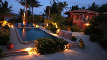 A swimming pool surrounded by palm trees and a red building.