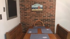 Un coin repas avec un mur en briques, une table en bois et quatre sets de table bleus.