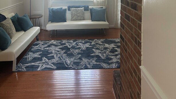 Un salon avec un canapé blanc, des coussins bleus, un tapis à motifs et un mur en briques.