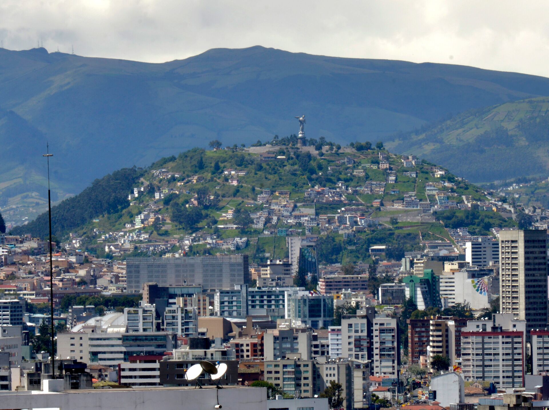 A cityscape with a prominent hill in the background, featuring a statue on top.