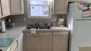 A kitchen with light wooden cabinets, a white refrigerator, a sink with a window above, and a wooden floor. - Family Friendly Townhome W/POOL In Ocean City, Md. (Ocean City)