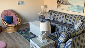 A cozy living room with a striped sofa, a wicker chair, a ceiling fan, and a beach-themed painting. - Family Friendly Townhome W/POOL In Ocean City, Md. (Ocean City)
