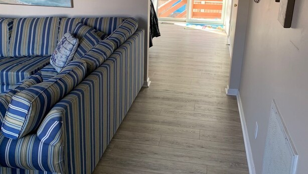 A living room with a striped sofa, a painting of a beach, and a view of a wooden deck and outdoor area. - Family Friendly Townhome W/POOL In Ocean City, Md. (Ocean City)