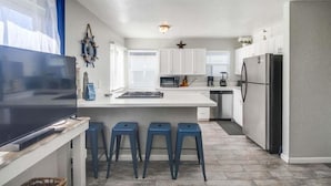 A modern kitchen with white cabinets, a large island with bar stools, a refrigerator, and a microwave. - Large 5 Bedroom House Beach side in Mission Beach (San Diego)