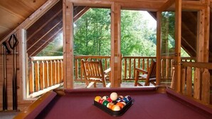 Ein Billardtisch in einem Holzraum mit großen Fenstern und einem Balkon.