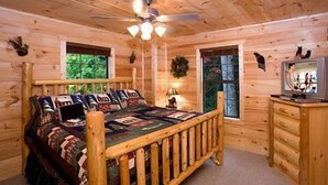 Ein Schlafzimmer einer Holzhütte mit einem Bett, einem Deckenventilator, einem Fernseher und einem Fenster.