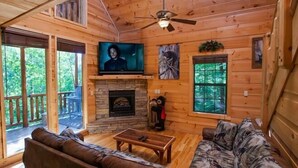 Ein gemütliches Blockhaus-Interieur mit Kamin aus Stein, Holzwänden, einer Ledersofa und einem Deckenventilator.